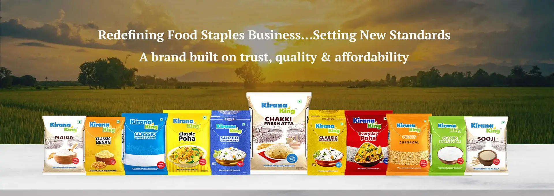 Sunrise over lush farmland with a wide view of nature’s bounty, featuring a vibrant array of Kirana King packaged staple grocery products—Chakki Fresh Atta, Rice, Sugar, Poha, Pulses, and Besan—symbolizing purity, freshness, and quality